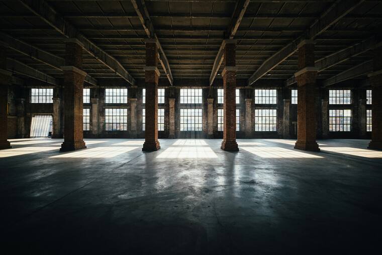 Große leere Industriehalle mit Backsteinpfeilern und Sonnenlicht